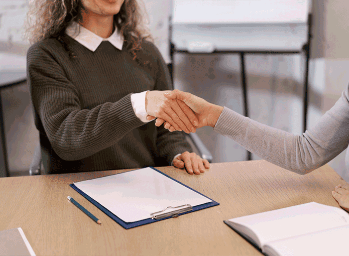 Duas mulhres apertando as mãos numa entrevista de emprego