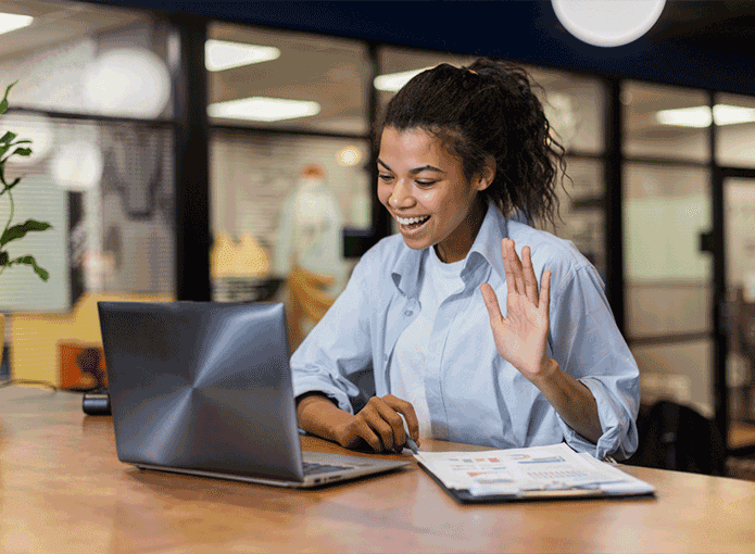 Mulher sentada cumprimentando alguém através da tela de um notebook