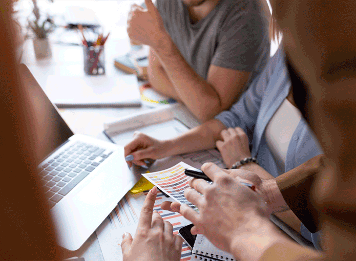 Um grupo de pessoas  sentadas a mesa em volta de um computador