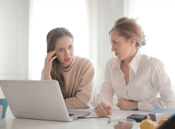 Duas mulheres sentadas à mesa olhando para um notebook