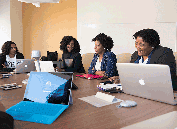 Um grupo de pessoas sentadas ao redor de uma mesa com notebooks